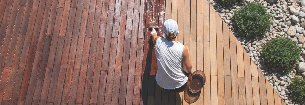 Person streicht Holzterrasse mit Pinsel